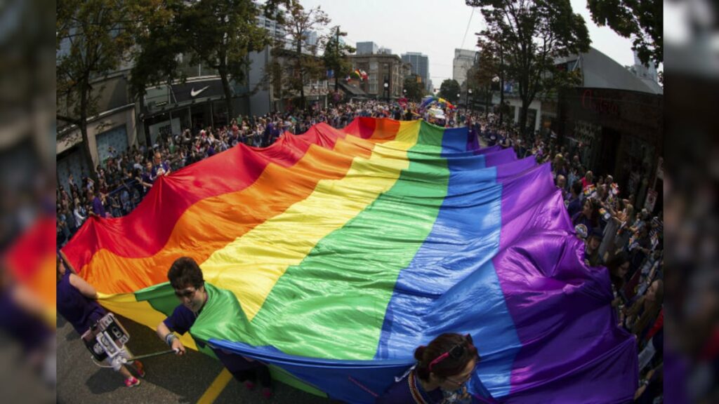 Rainbow flag flying across and caught by human around in the midst of queer pride march