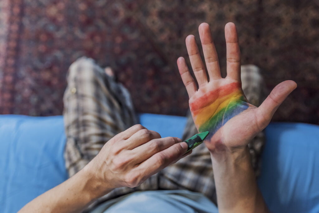 View from above of Person or activist painting rainbow on hand palm for St Valentine's Day. Closeup of a young Caucasian man with rainbow flag painted in his palm, emerging from darkness.