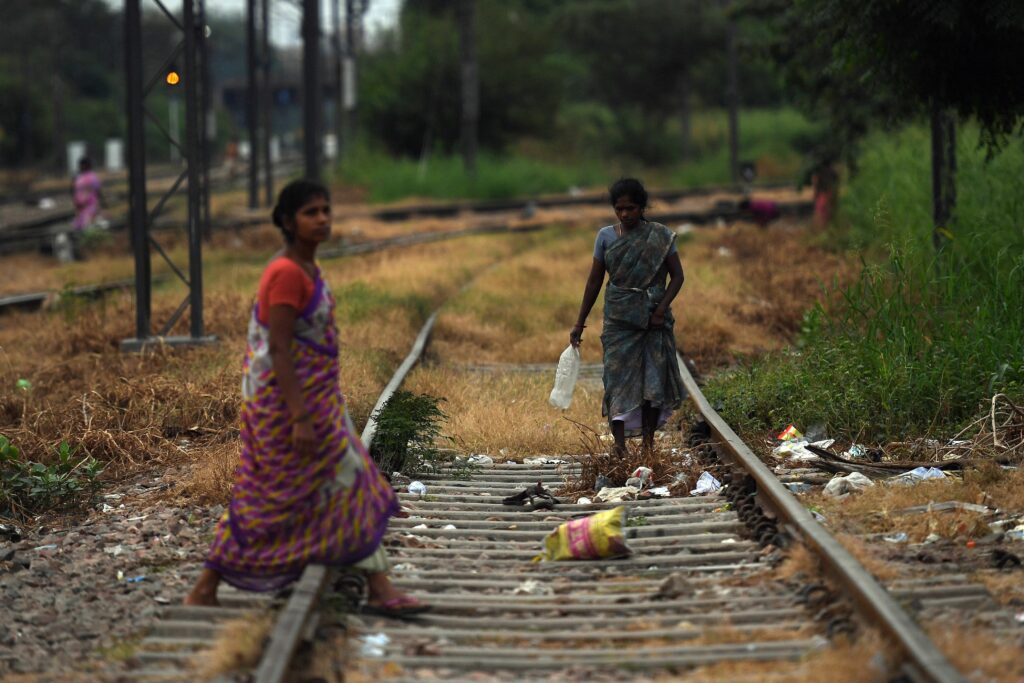 Two women walking on railway tracks  with one holding a water bottle in hand