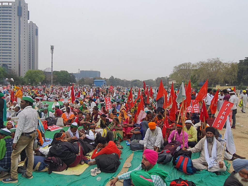 Hundreds of men and women farmers sitting on ground with red flags in hands