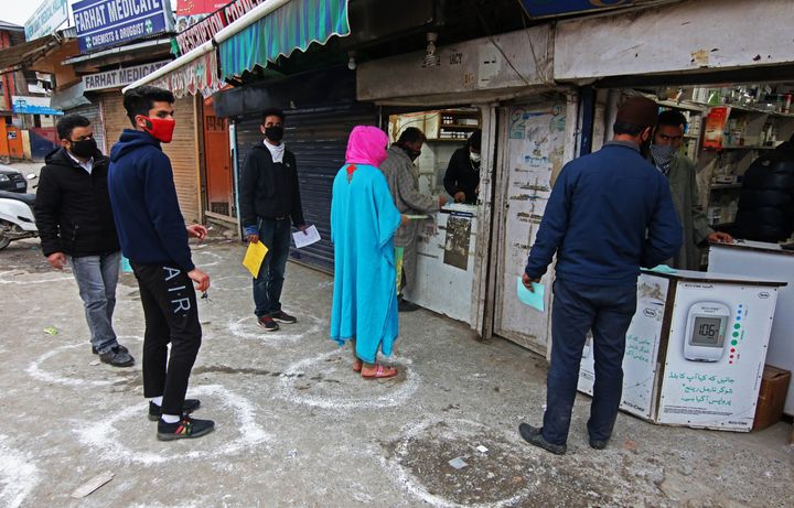 Kashmiri woman in blue dress and red scarf outside a medical store 