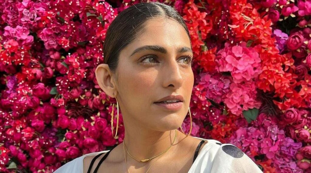 Kubbra Sait posing for a photo with a background of read and pink flowers 
