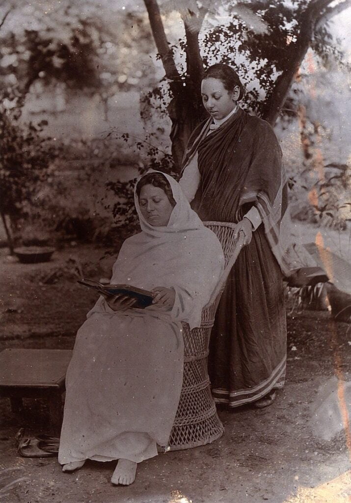 Pandita Ramabai on a wooden chair with a woman standing behind the chair 