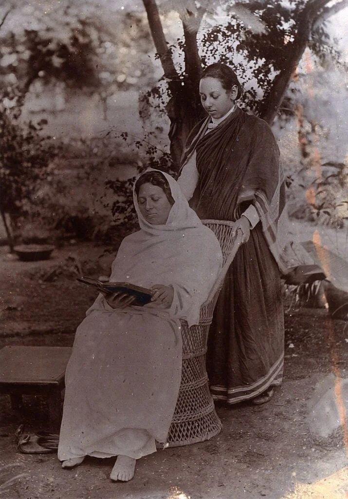 Pandita Ramabai on a wooden chair with a woman standing behind the chair