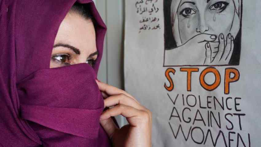 Kashmiri woman hiding her face standing next to a "stop violence against women' sign. 