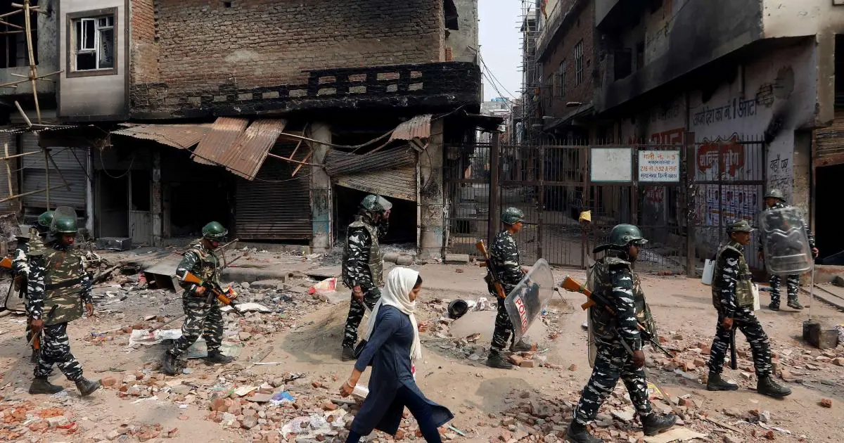 A woman walks past security forces patrolling a street in a riot affected area in New Delhi, India, February 26, 2020.